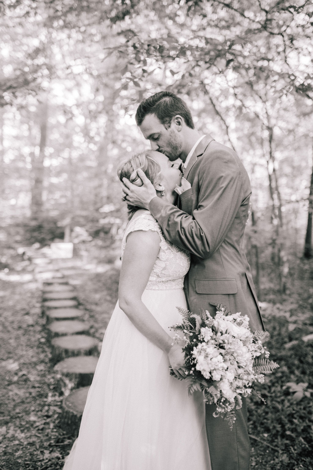black and white photo of a bride and groom standing on tree stumps and embraceing each other in the woods of the Ijams for their destination wedding