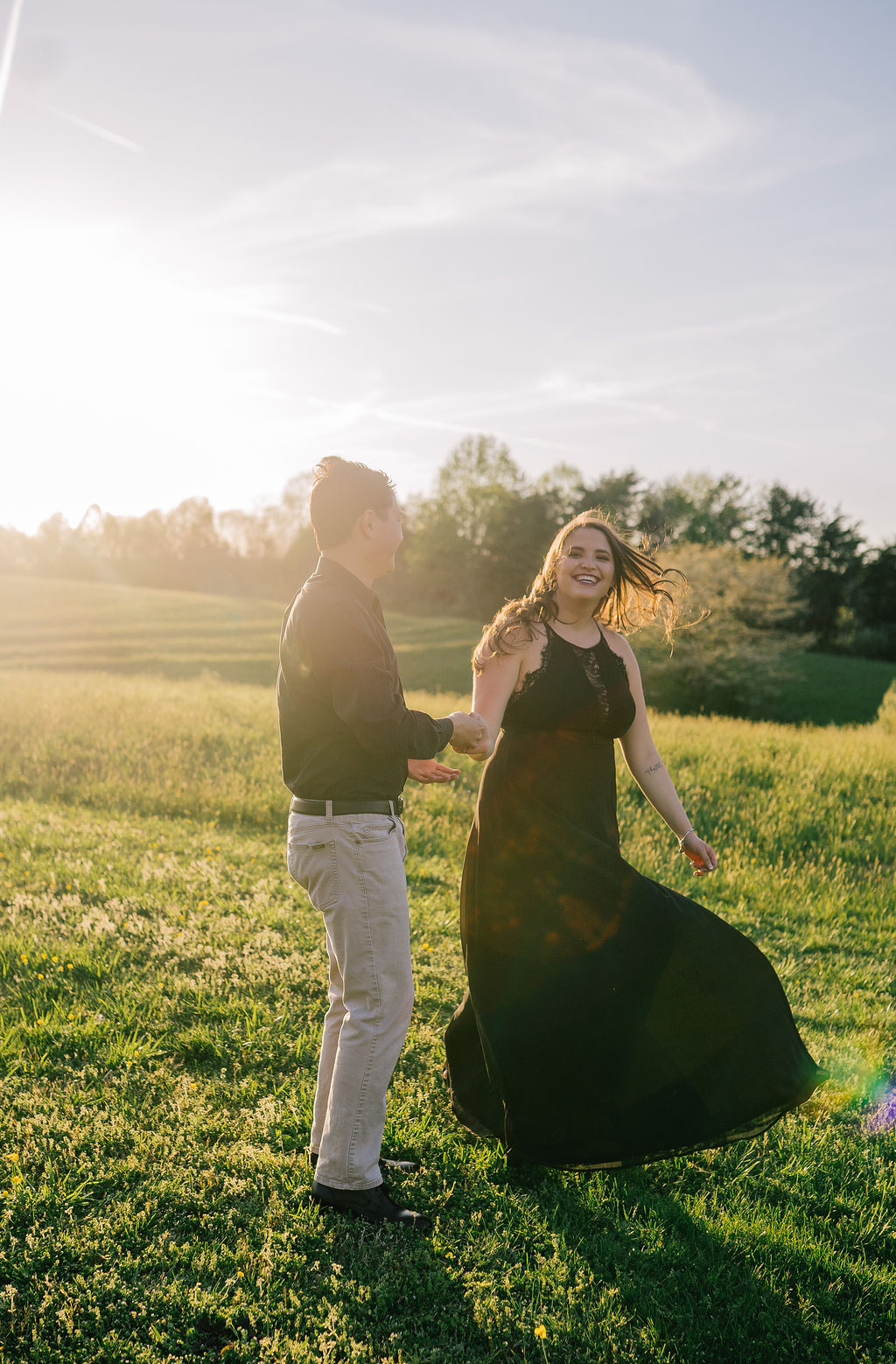 sun setting at Meads Quarry in Tennessee as a man and woman dancing in a green grassy field while wearing all black for their engagement session