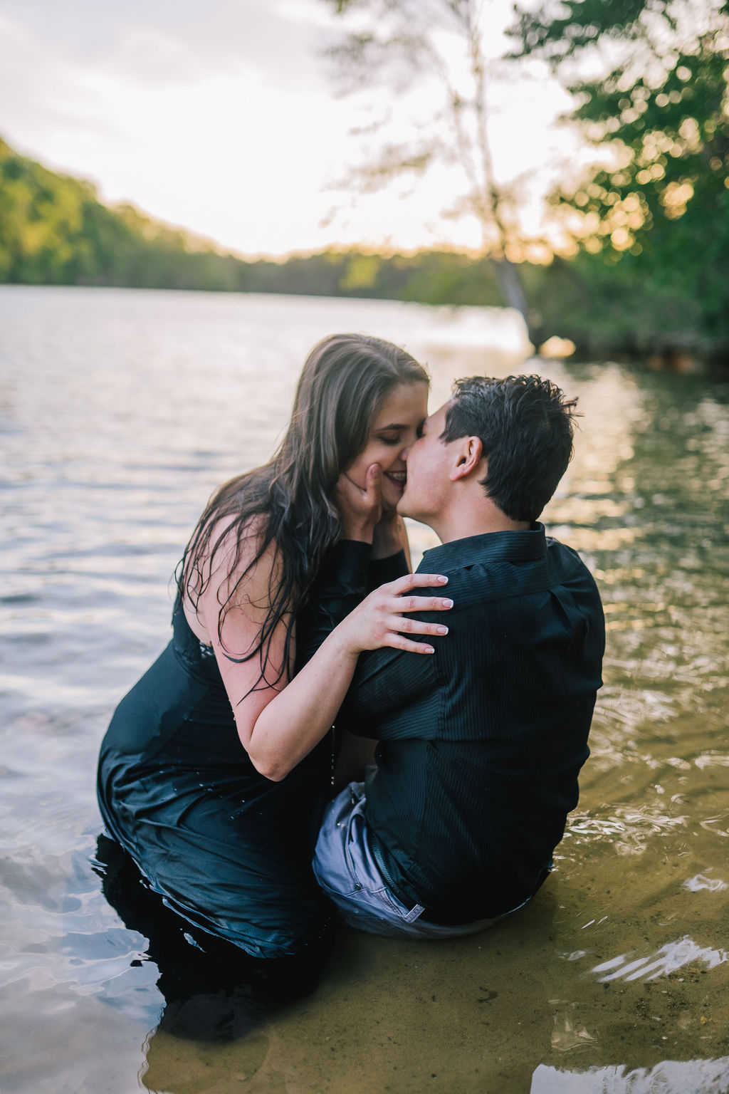man and woman sitting in the water for their Meads Quarry engagement session with the woman on top of the man holding his shoulders and kissing him as he holding her face