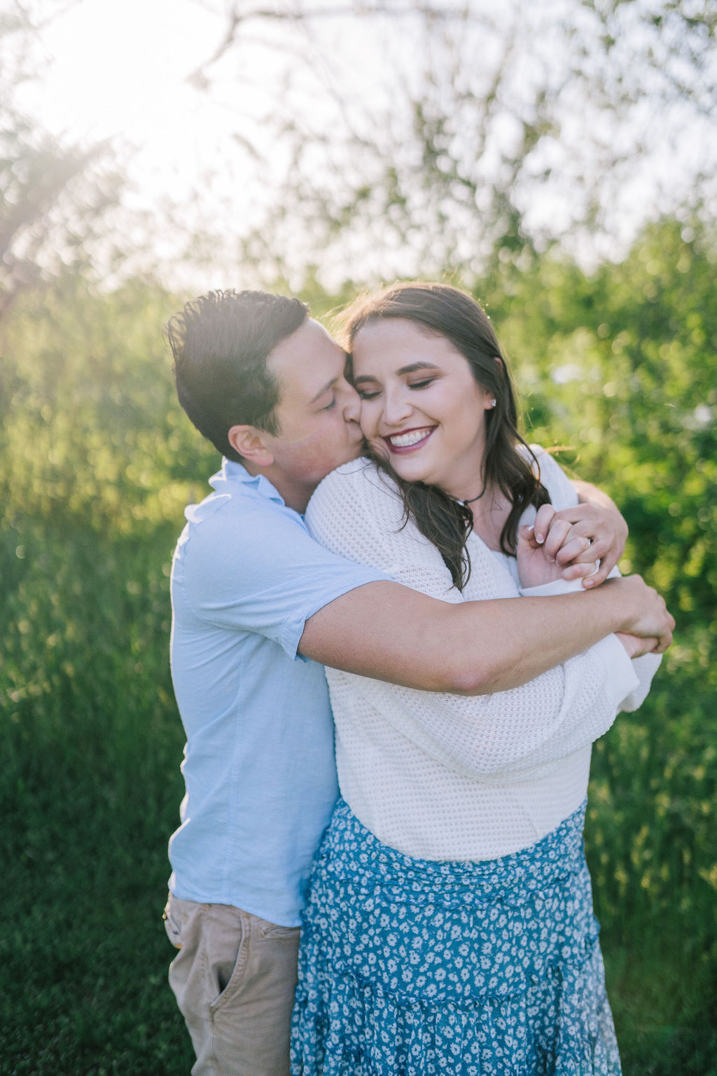 man hugging woman from behind as she looking back at him and smiles as her goes into kiss her cheek