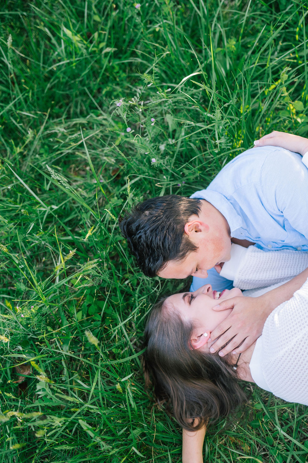 green grassy behind a man and woman as they lay on their sides and cuddle for a romantic outdoor engagement photo