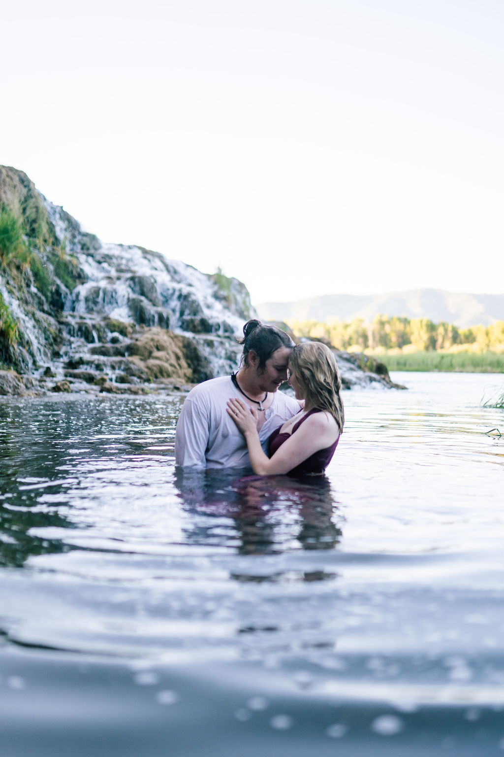 engagement session in a lake at some waterfalls in the Smokies with man and woman sitting in the water and embracing each other romantically