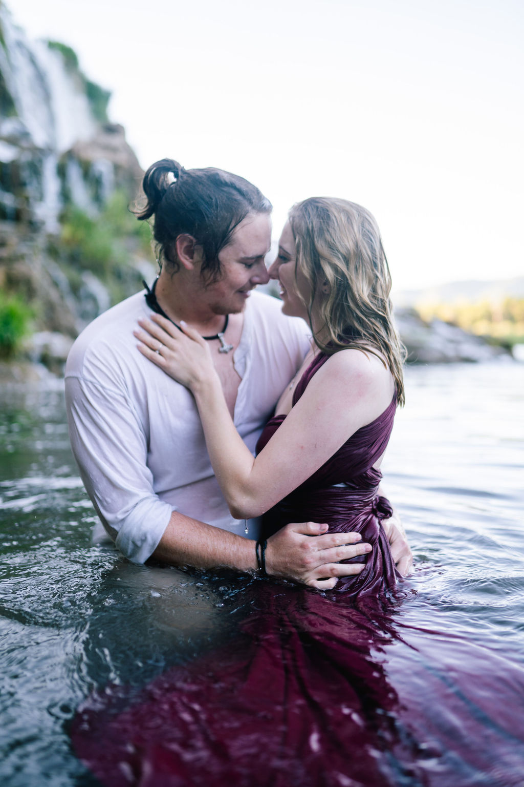 waterfall engagement session in TEnnessee with man and woman sitting in a pond together holding each other while completely soaked
