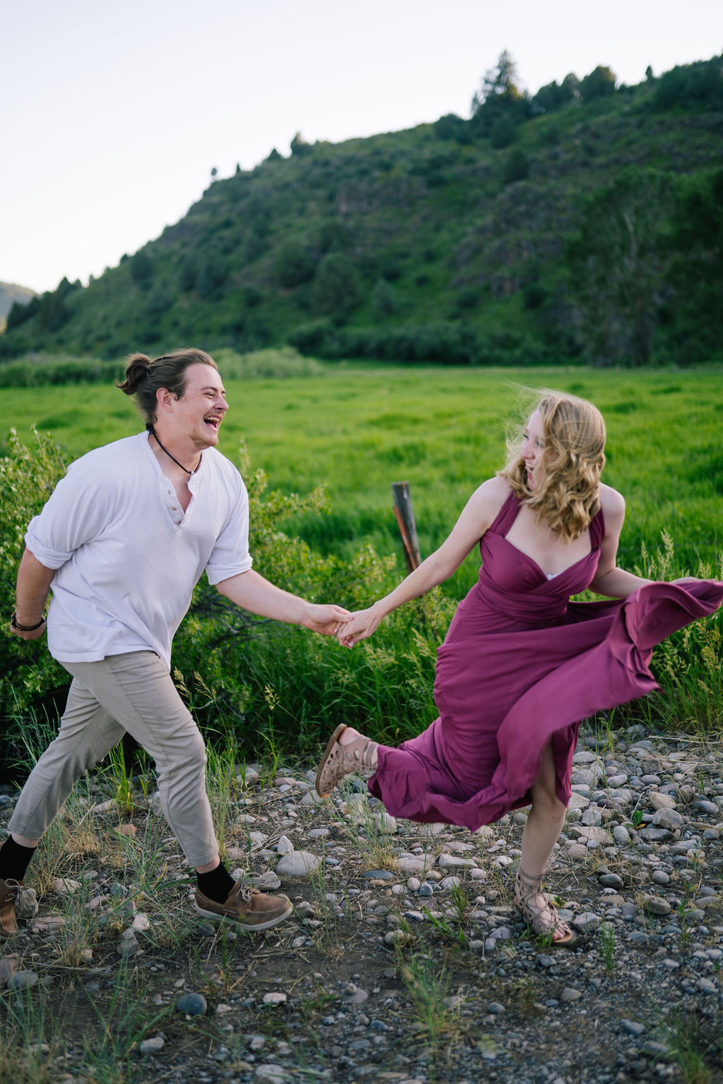 young couple holding hands and running through a green field in Tennessee for their engagement session in the summer