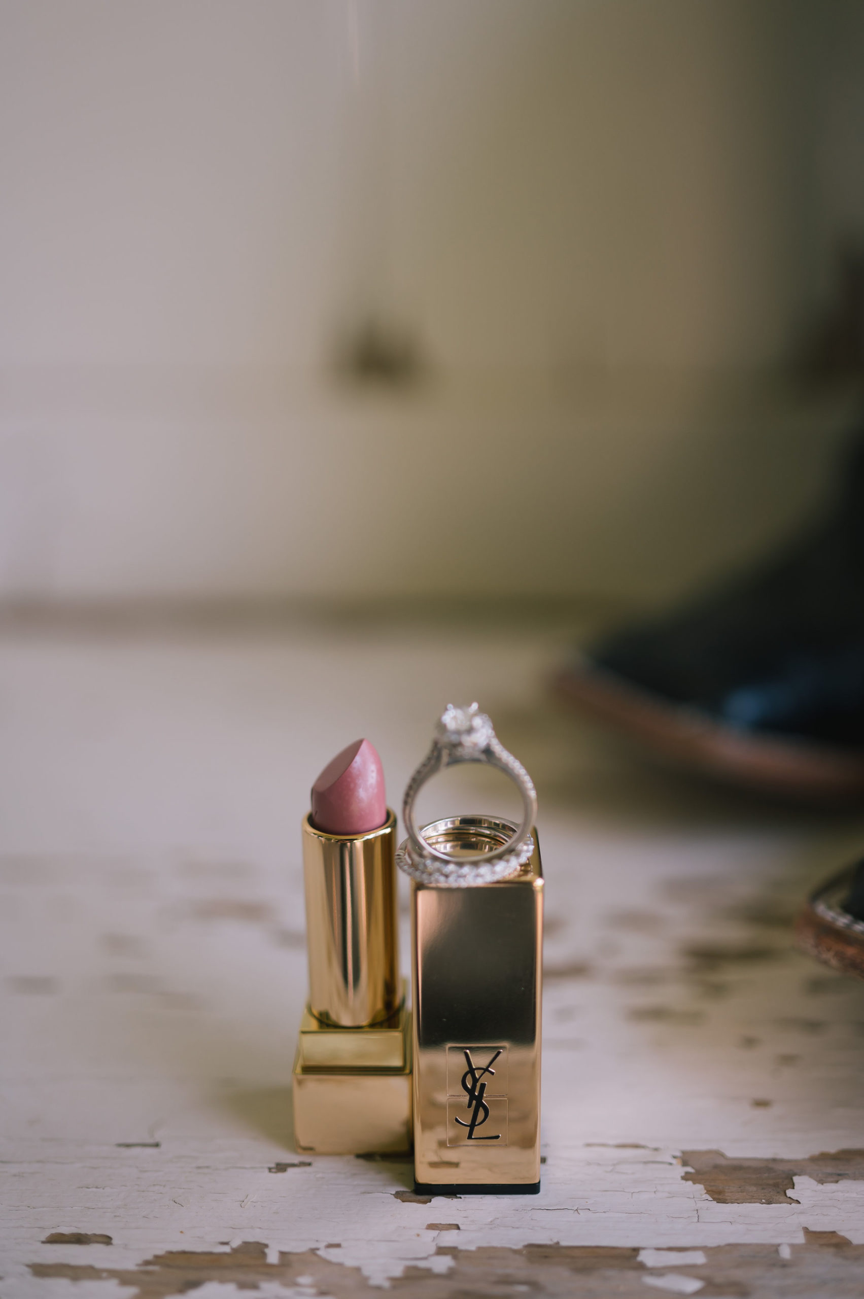 bridal flatlay photo with the brides wedding band and engagement ring balancing on a tube of lipstick