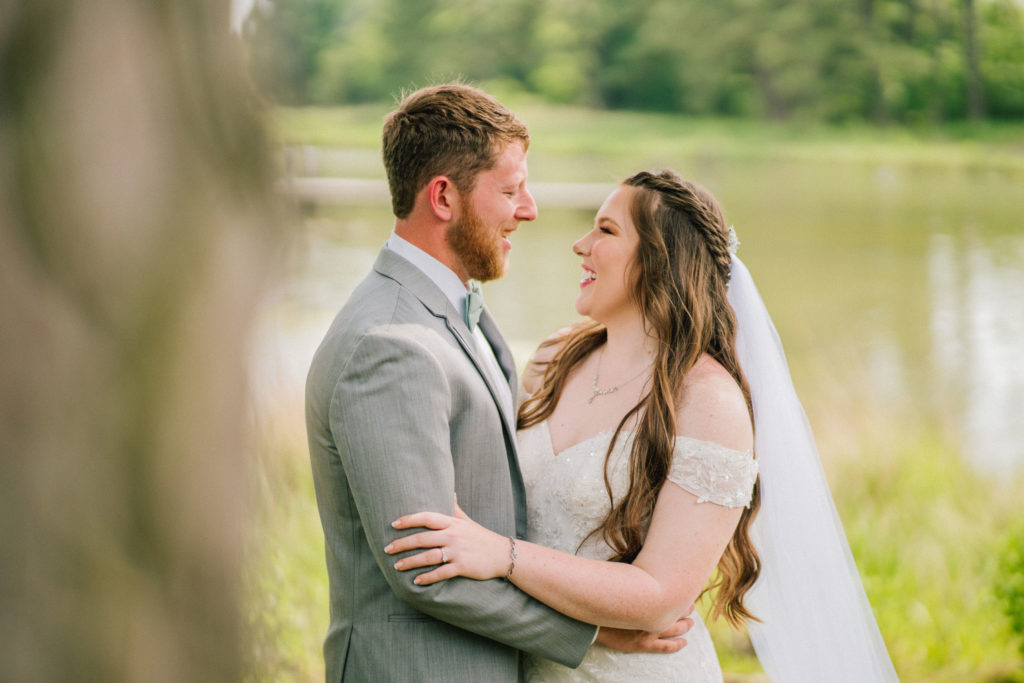 Maryland destination wedding bride and groom holding each other at the arms while standing next to a river as they look at each other and smile
