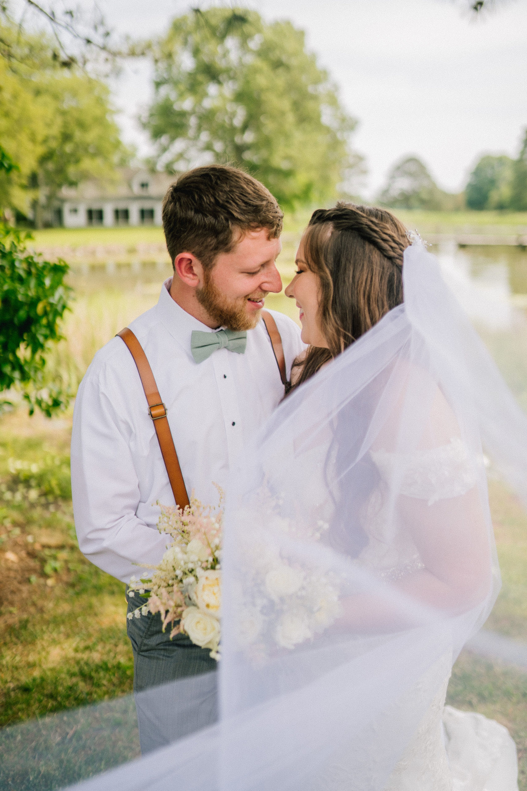 wedding day photos with bride and groom embracing each other and looking romantically into each others eyes with a lake behind them and bright green trees and foliage surrounding them