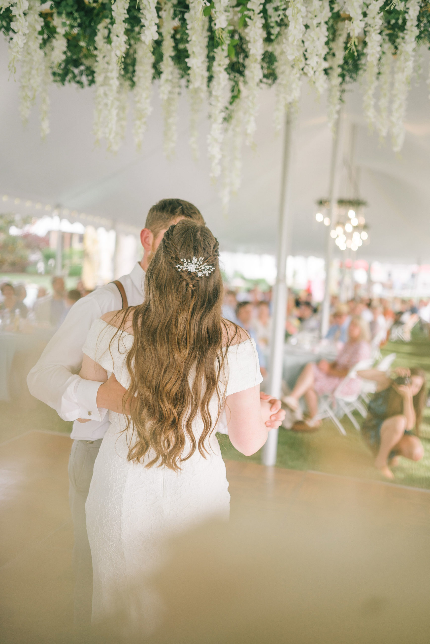 bride and groom have their first dance ina white tent with a floral chandelier hanging above them