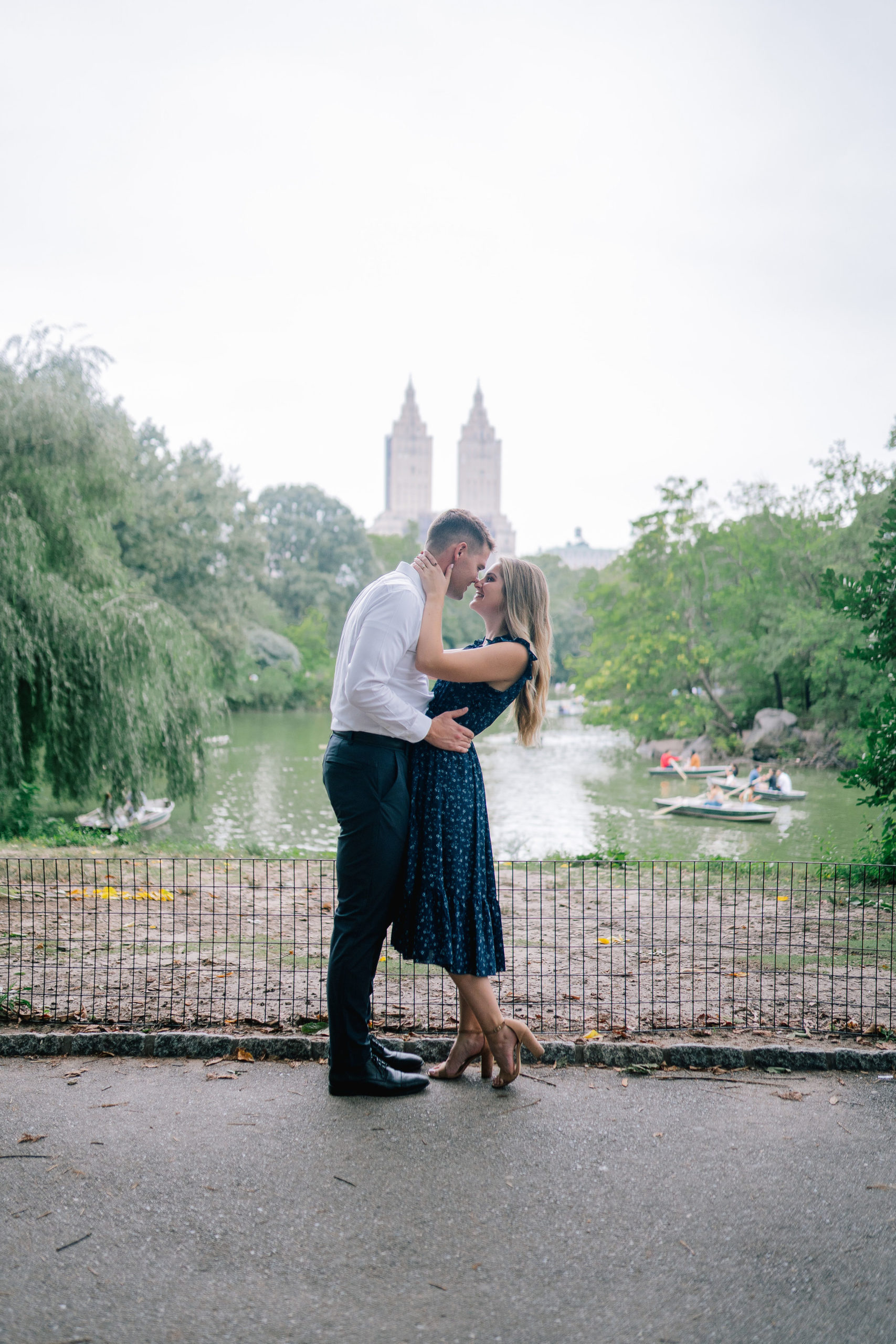 man and woman embracing each other in NYC Central Park with mans hands around the woman waist and the woman holding the mans face as they both smile and their noses touch, image captured by Manhattan wedding photographers