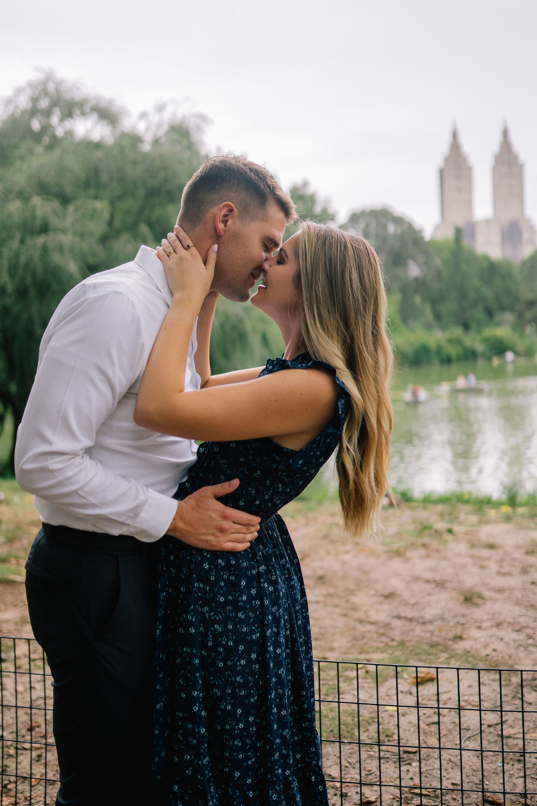man holding woman by the waist and leaning in to kiss her in front of the Leob boathouse in Central Park in Manhattan for engagement photos