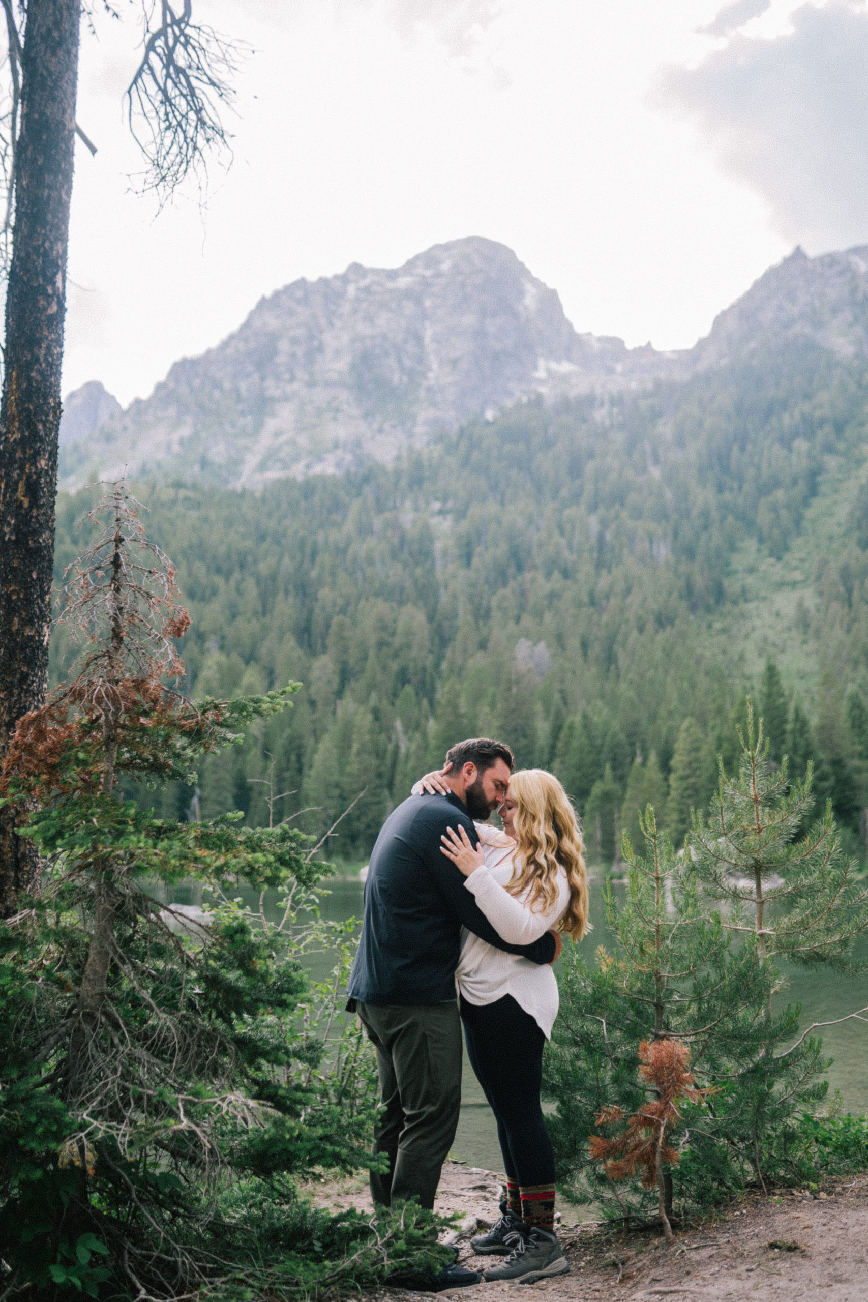 man and woman embracing one another next to a lake in the Smokies for their engagement session in the winter casual winter engagement photo outfits
