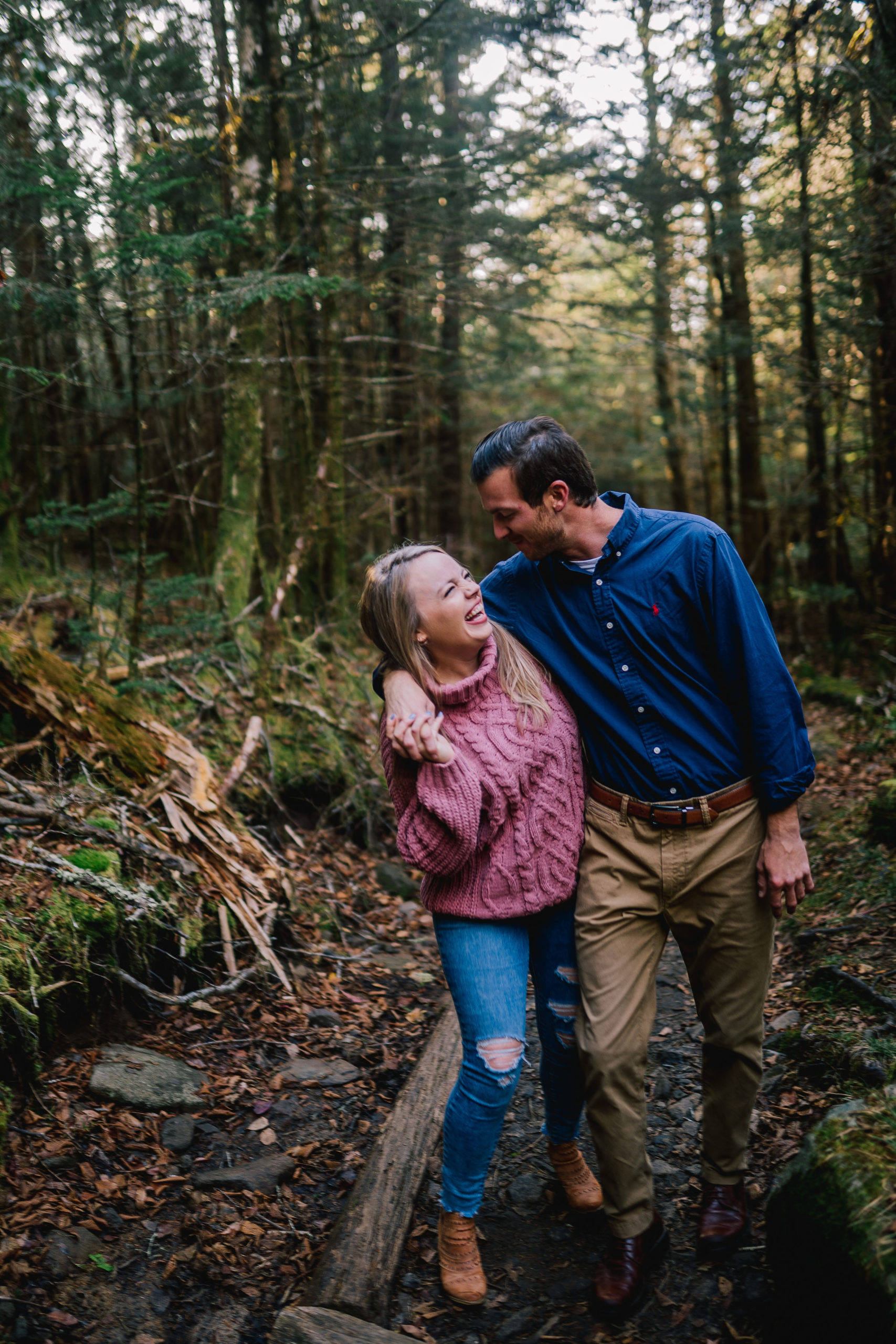 couple laughing as they walk down a dirt trail while the man holds the woman around the shoulder, casual winter engagement photo outfits