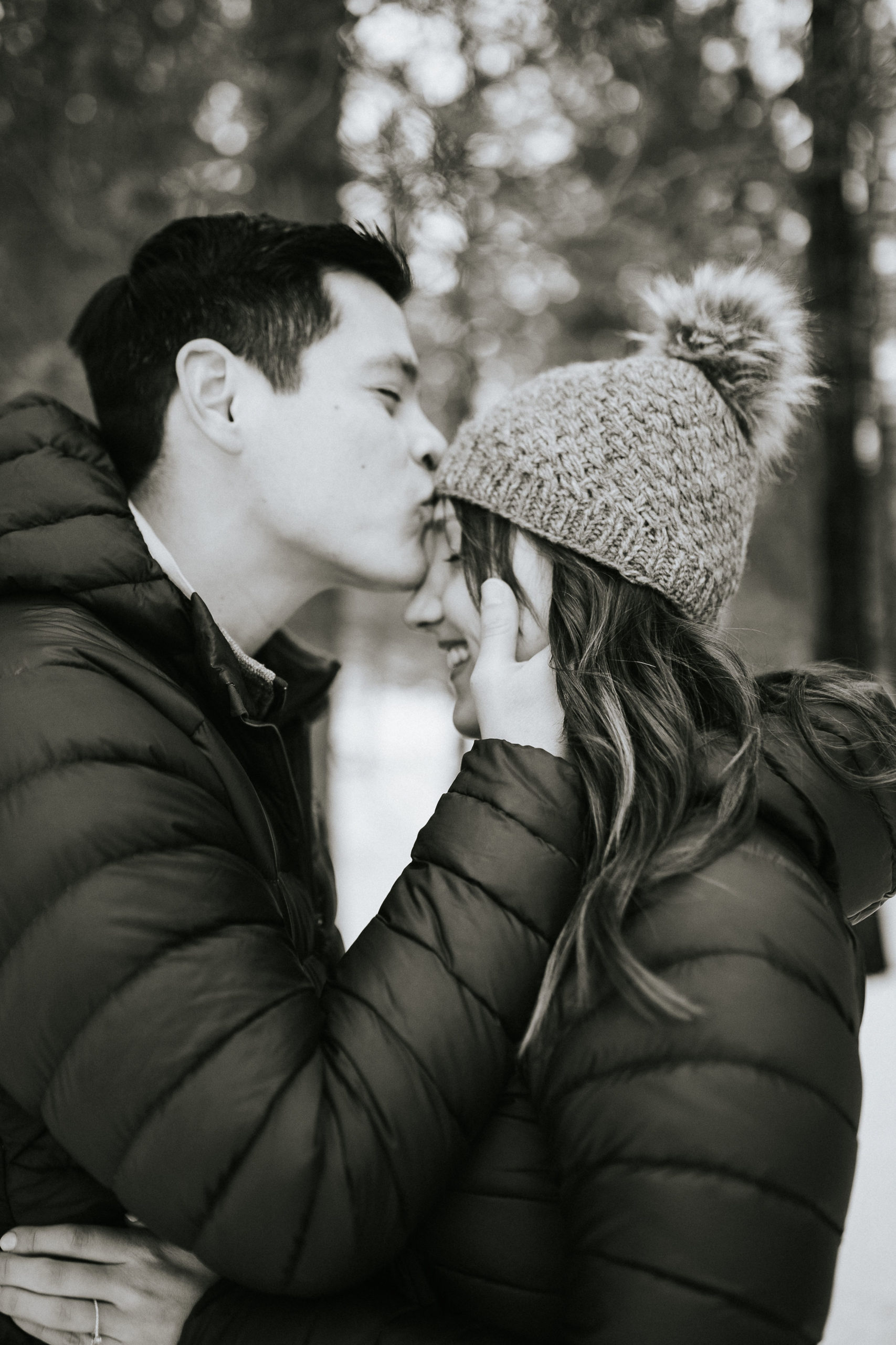 casual winter engagement photo outfits inspo with couple in snow coats in the SMokies with the man holding the womans head as he kisses her forehead as she wears a cute beenie hat, black and white engagement images