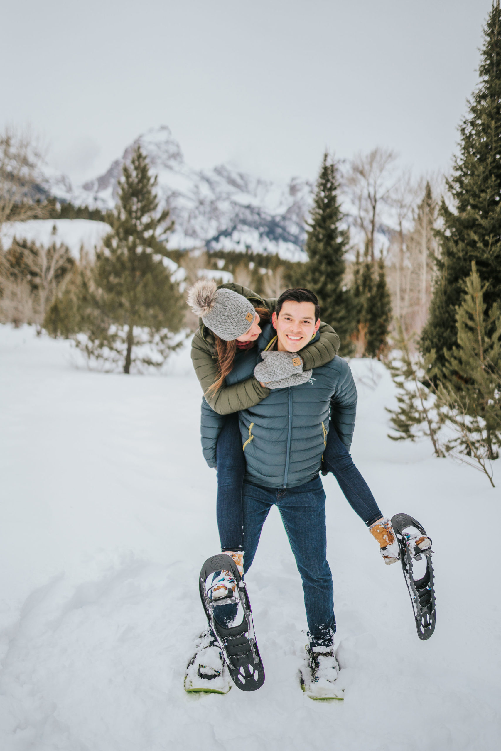 woman piggy backing on a man as they track through the snow in the mountain of Tennessee for their romantic winter engagement photos