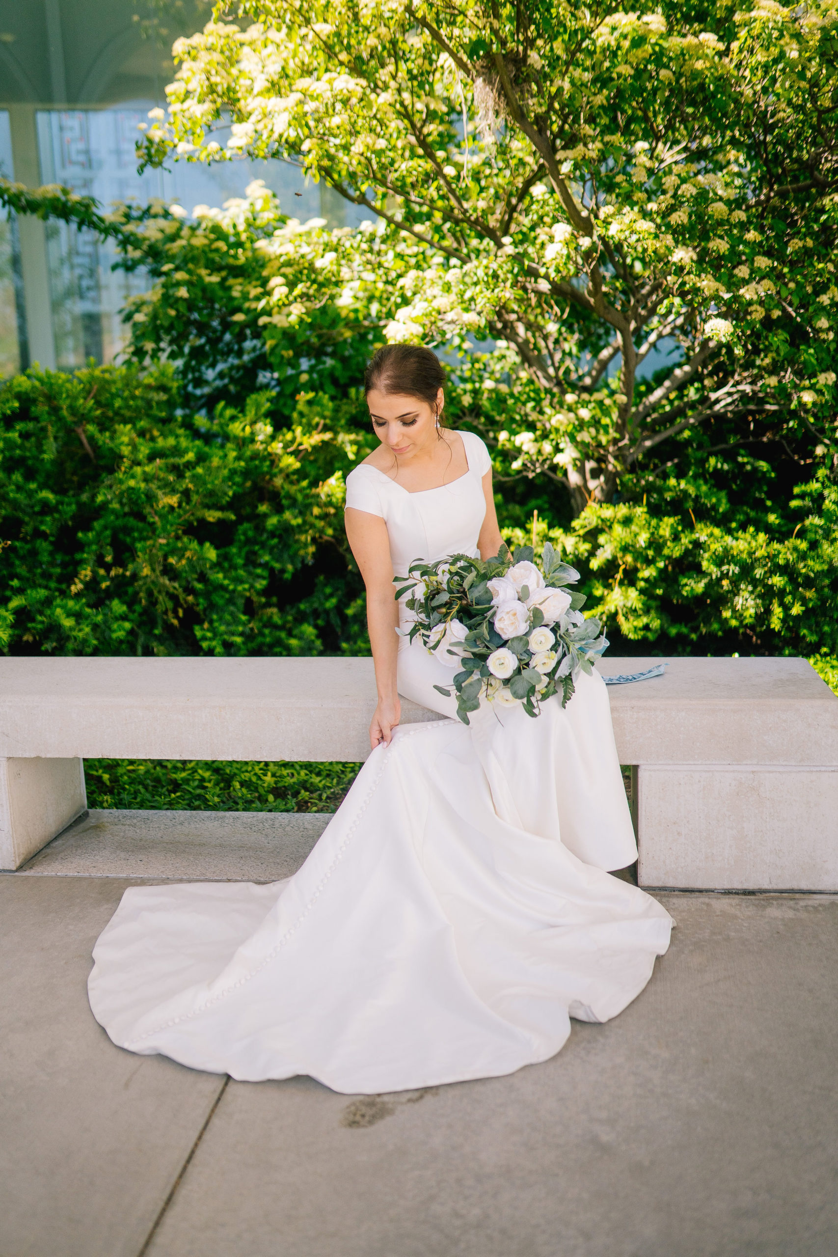 Amalfi Coast Themed Wedding Italian bride adjustng her dress as she sits outside of the temple in Utah with her bouquet of florals