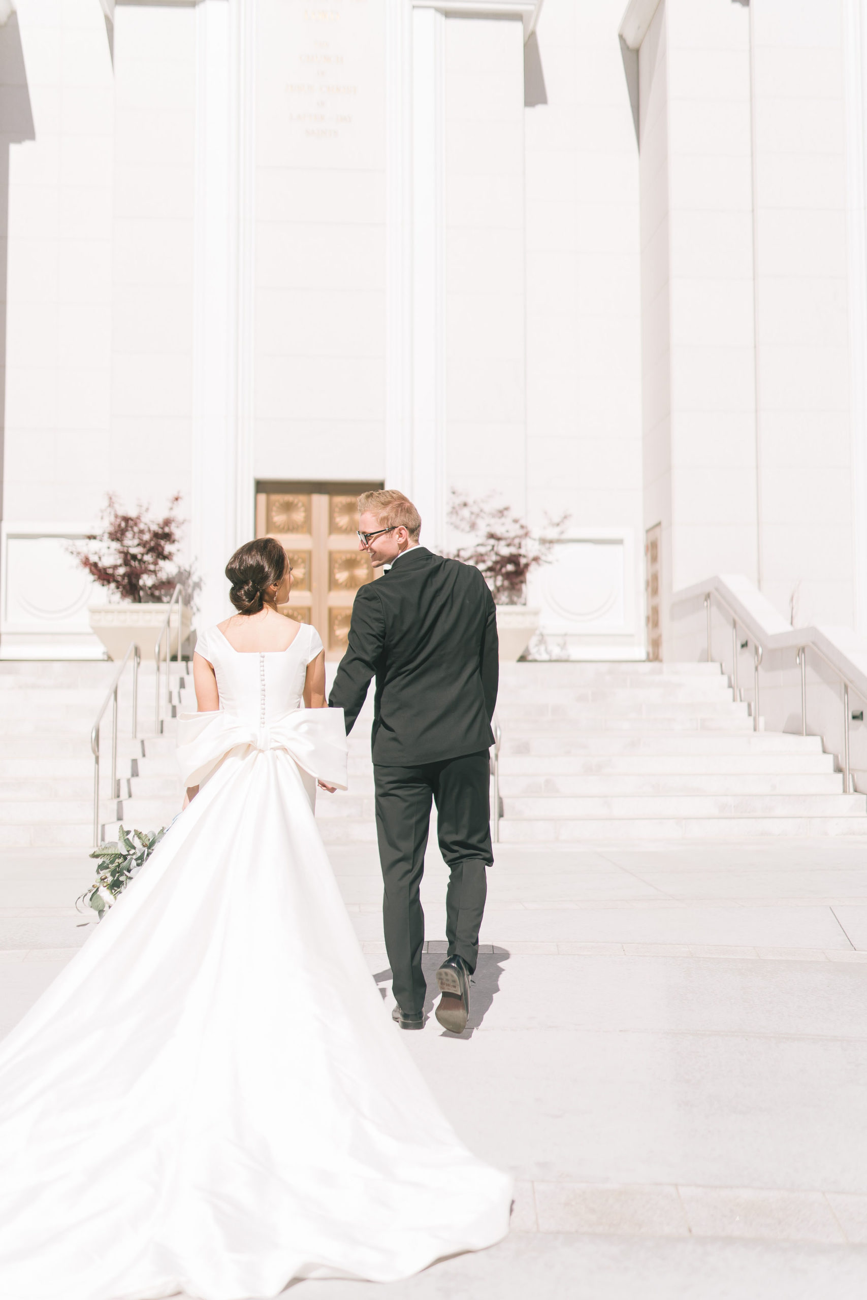 Wedding Photographers Sacramento captures Amalfi Coast Themed Wedding bright beautiful Italian wedding picture of bride holding hands with her towards an lds temple in Utah as they look to each other and smile