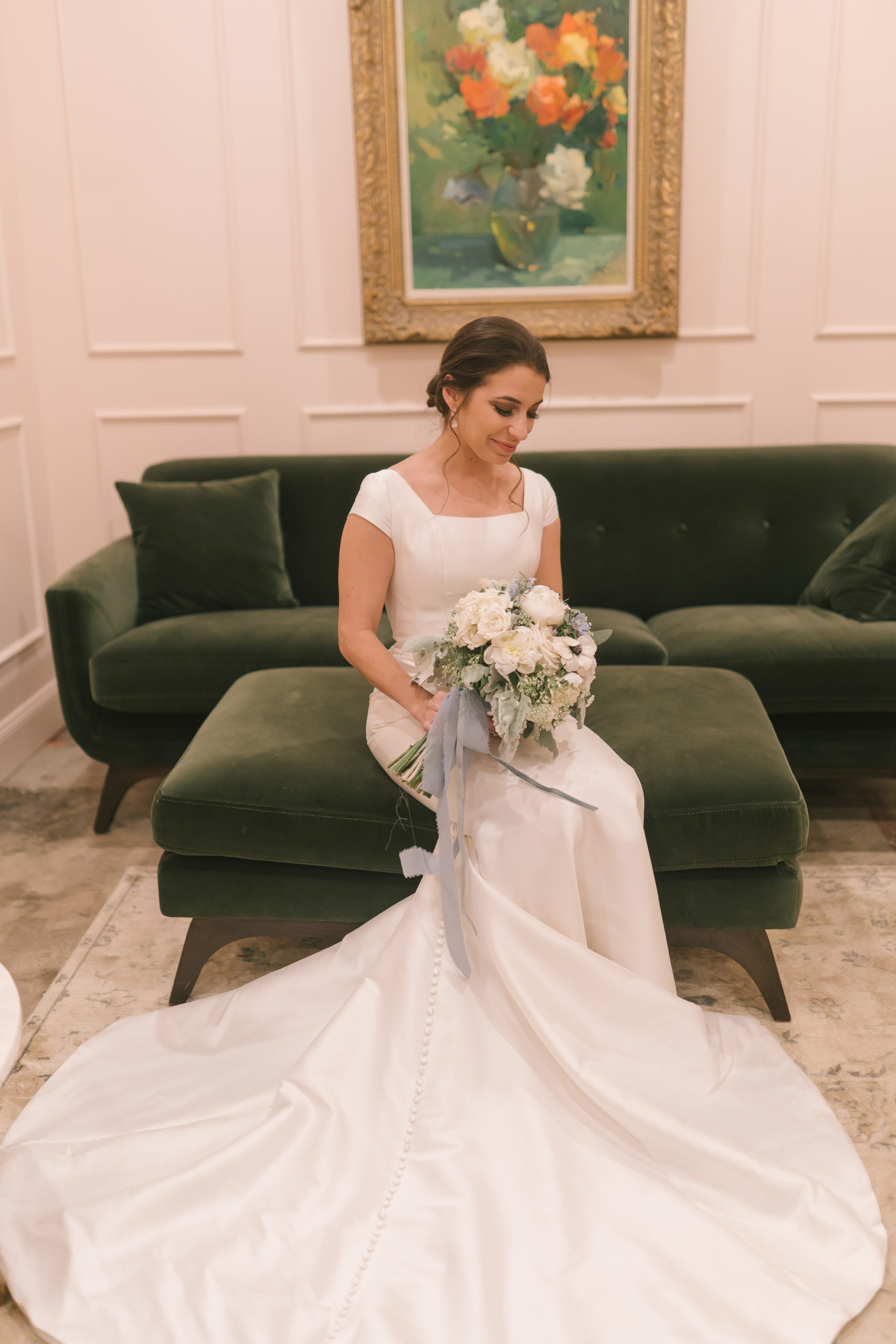 Amalfi Coast Themed Wedding Italian bride sitting on an emerald green sofa before her wedding in her bridal suite looking at her wedding bouquet and slightly smiling
