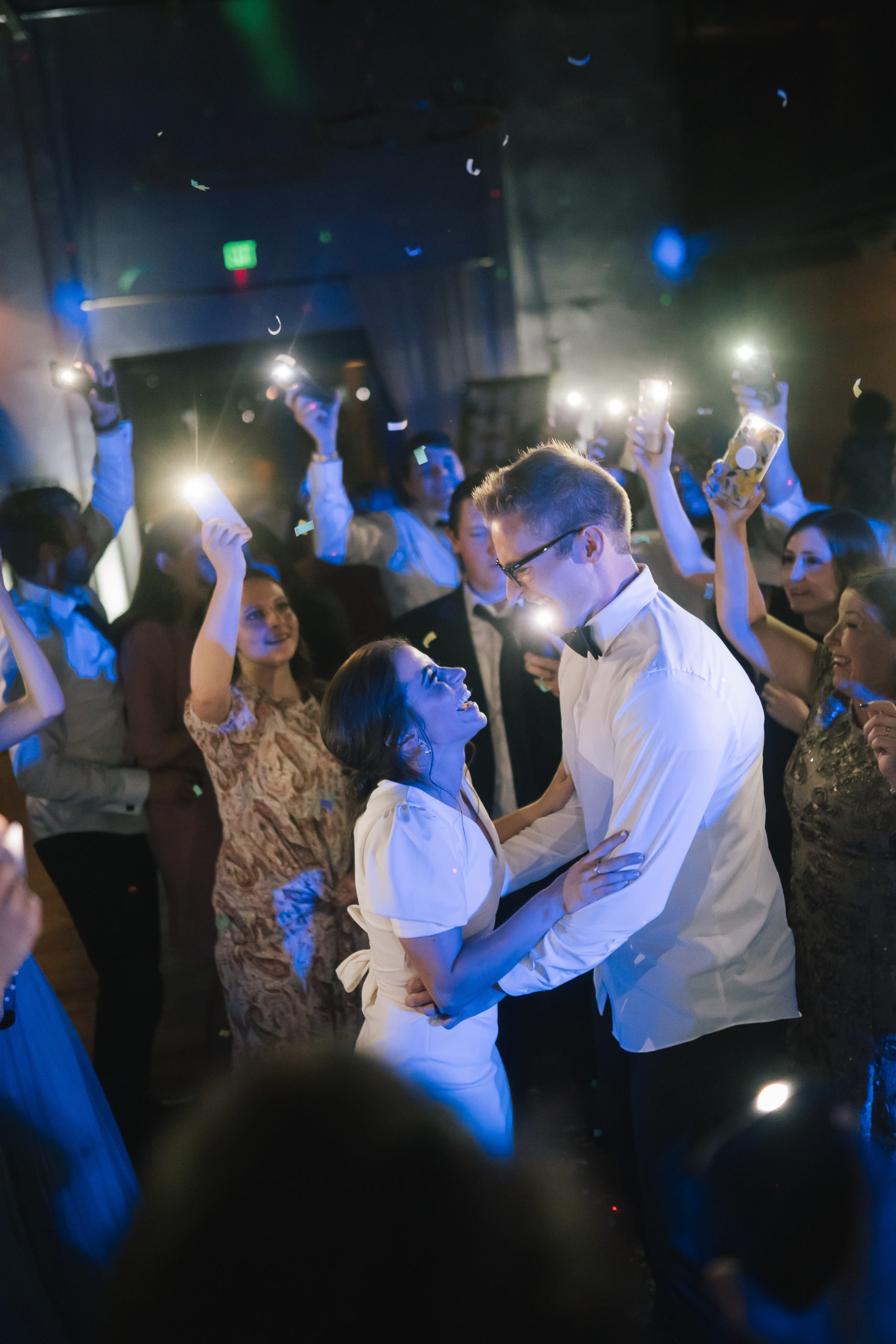 reception party with bride and groom dancing and everyone around them holding their phone cameras in the air