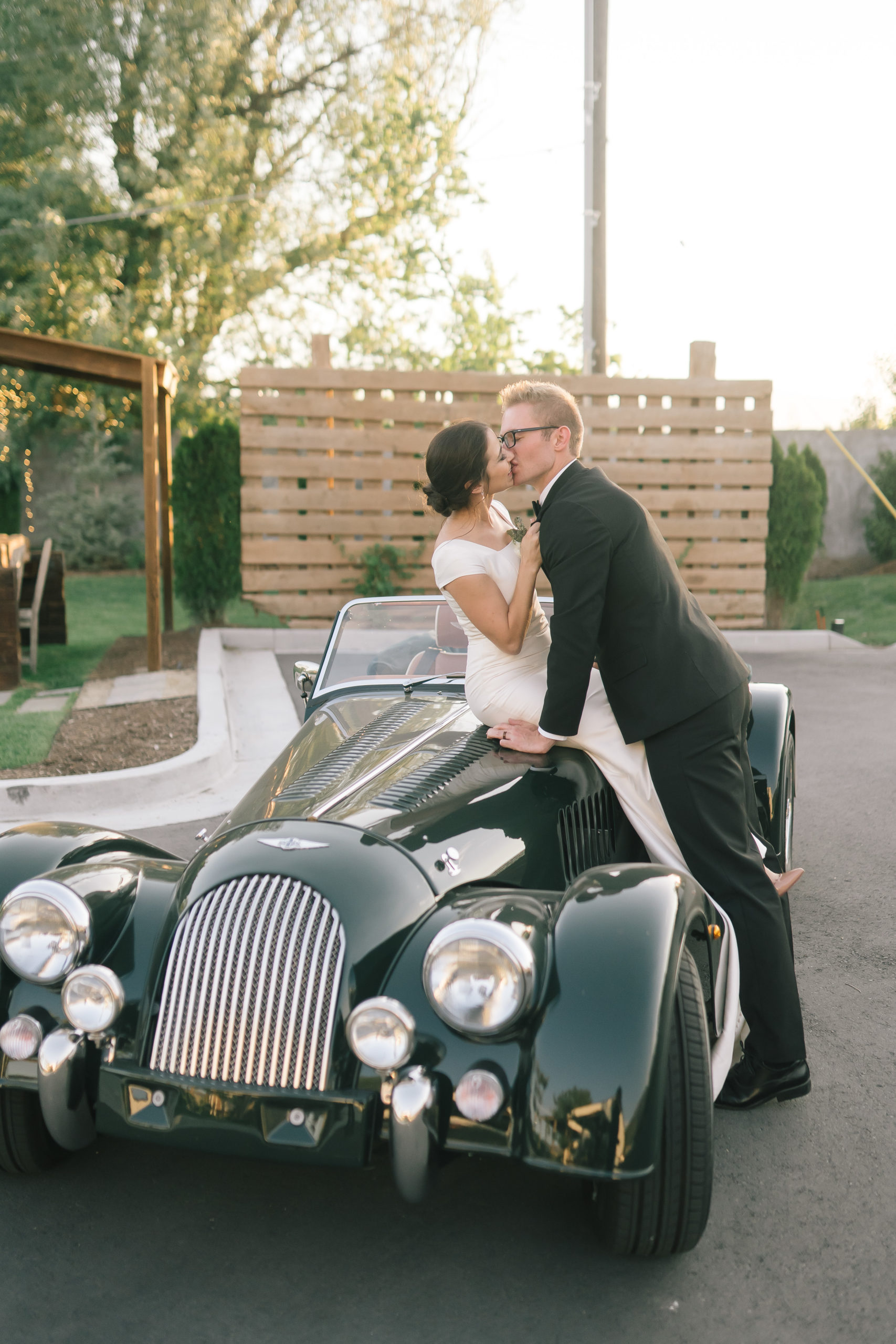 bride sitting on top of this emerald green vintage car and groom leaning over her to passionately kiss her
