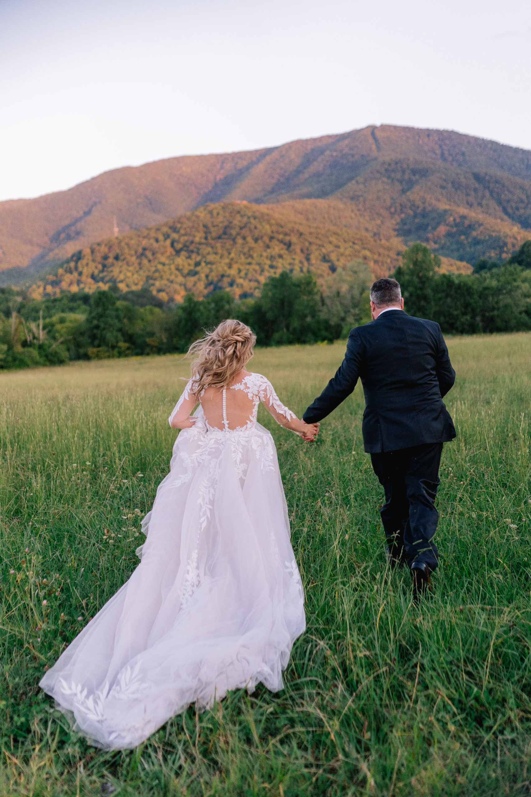 bride and groom in Pigeon Forge running through a field in the valley of the Smokies for their Tennessee wedding