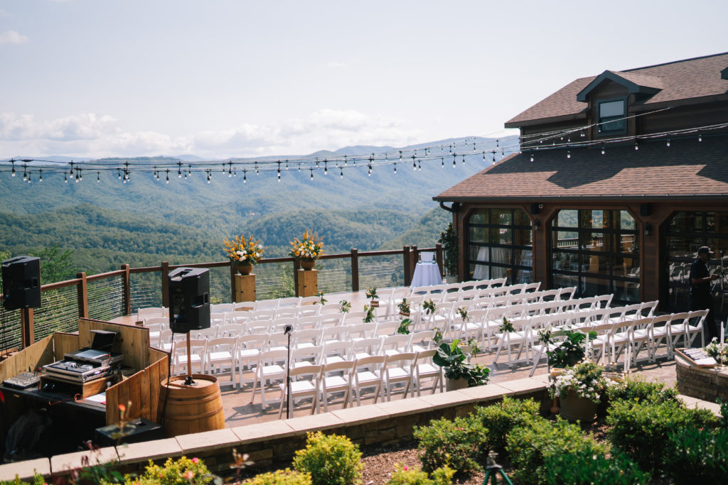 outdoor ceremony space at the Magnolia wedding venue pigeon forge with darling white chairs and strings of Edison bulbs with the Smokies in the distance